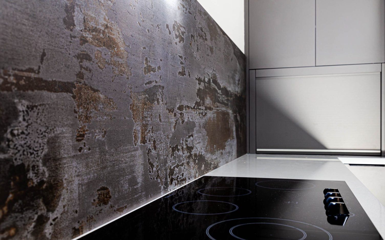 Trilium Porcelain splashback panel behind a ceramic hob with a worktop edge and light wall return visible on the right