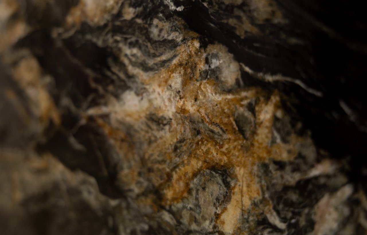 Macro close up of African Fusion Granite showing swirling gold veining and layered natural stone patterning in dark tones.