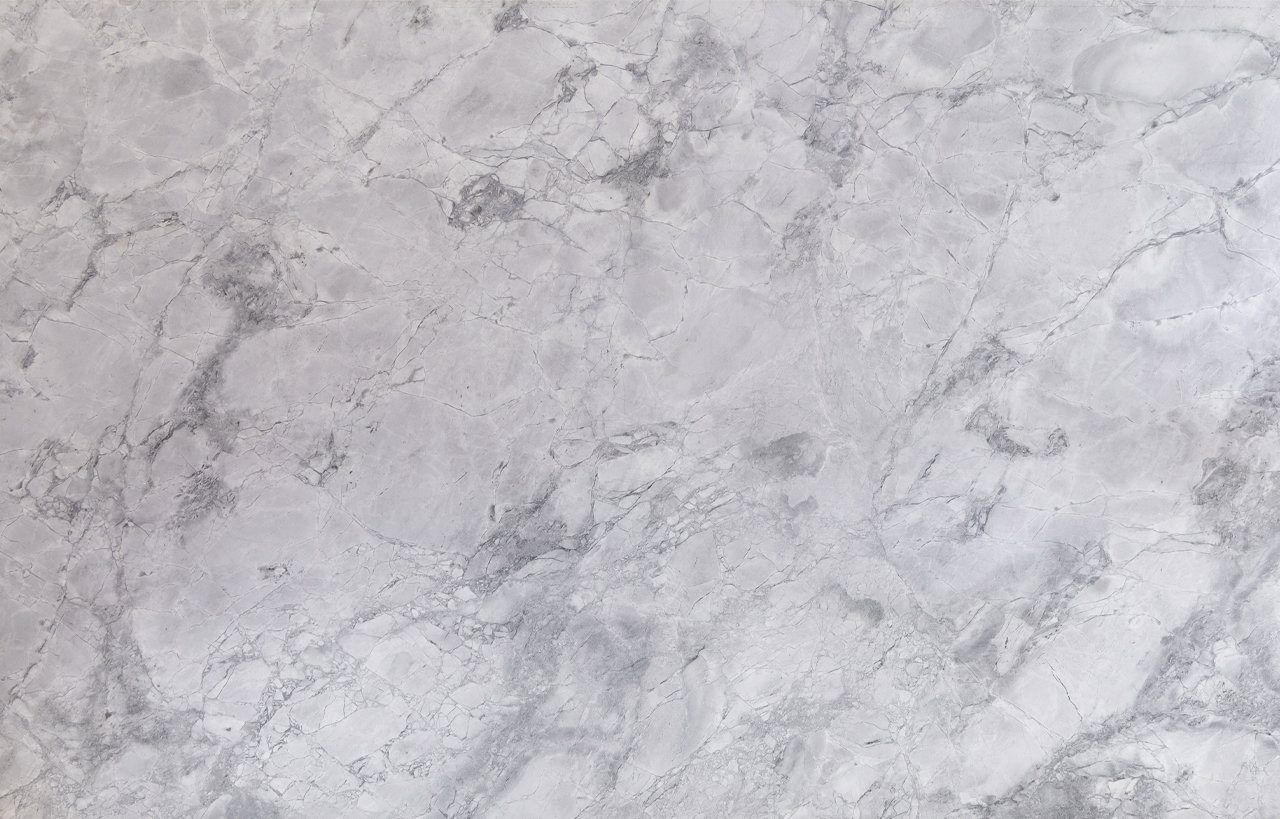 Close up slab photo of Bianco Eclipsia Granite showing soft pale grey clouding and gentle natural movement across a light stone surface.