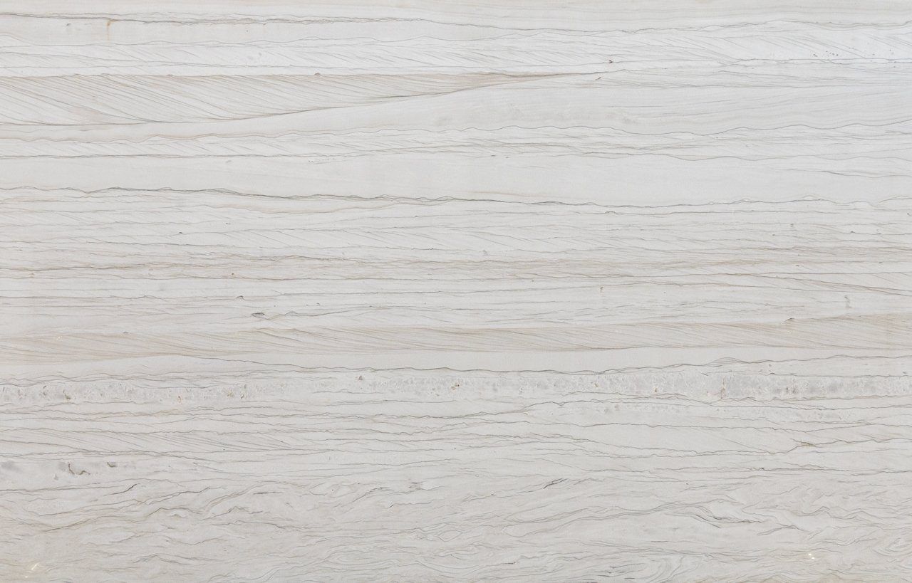 Close up slab photo of Bianco Macaubas Granite showing fine linear grey veining and a subtle grain across a pale stone surface.