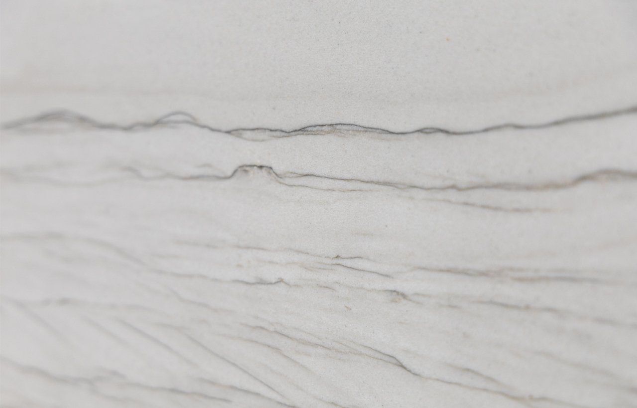 Close up slab photo of Bianco Macaubas Granite showing soft horizontal grey veining across a pale stone background with gentle layered movement.