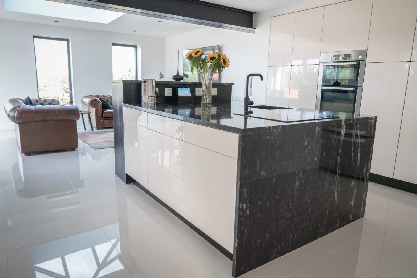 Side view of a modern kitchen with Cosmic Black Granite worktops on the island and perimeter run, showing waterfall ends and a polished surface finish.
