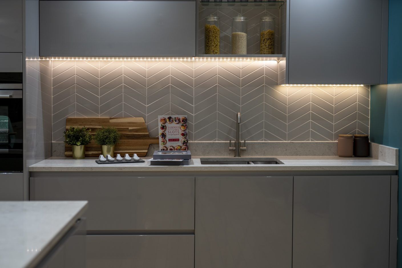 Grey Drift Quartz worktop run with undermount sink and lit splashback in a modern kitchen