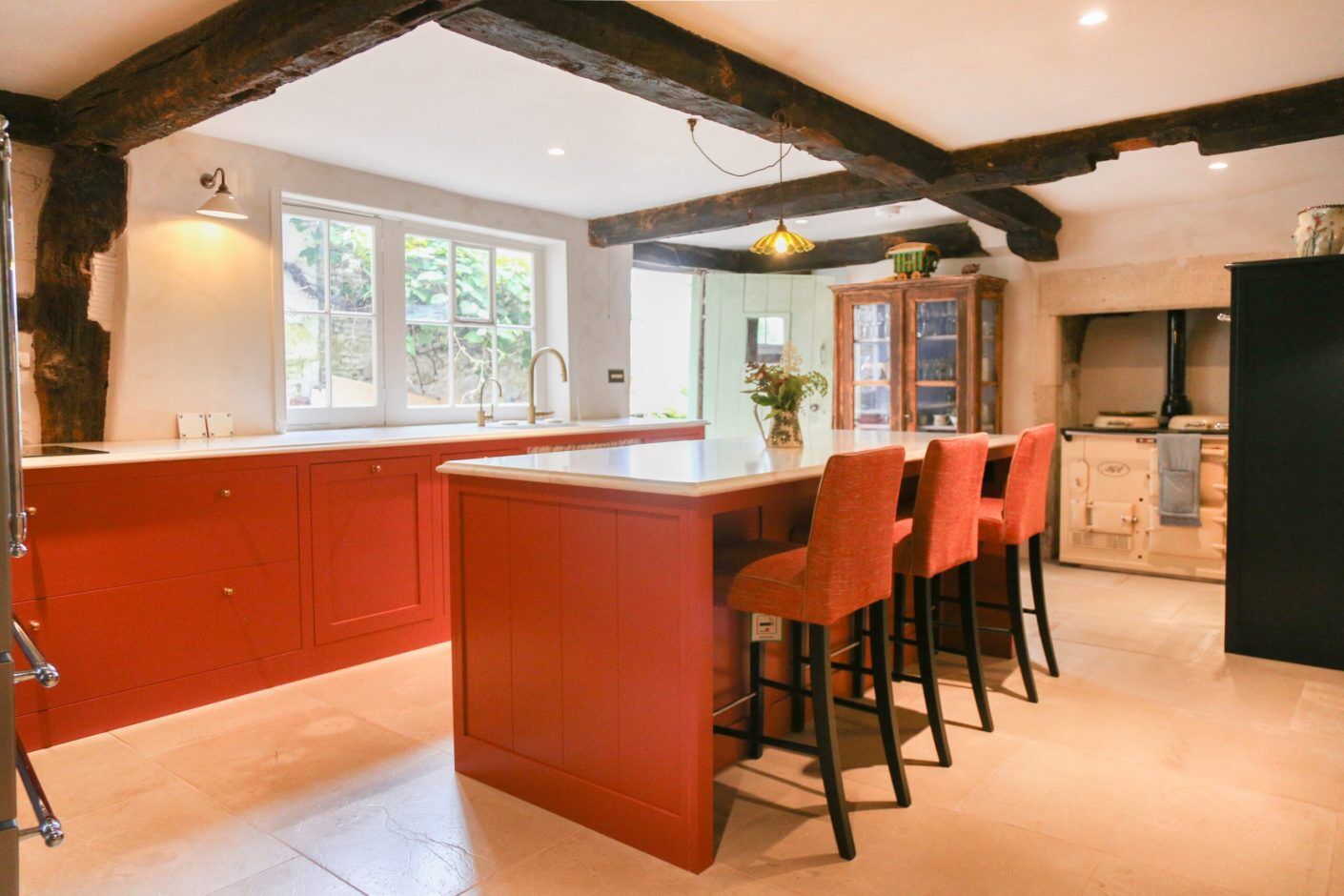 Open-plan kitchen with Supreme Calacatta Quartz island and breakfast bar seating on red cabinetry and exposed beams