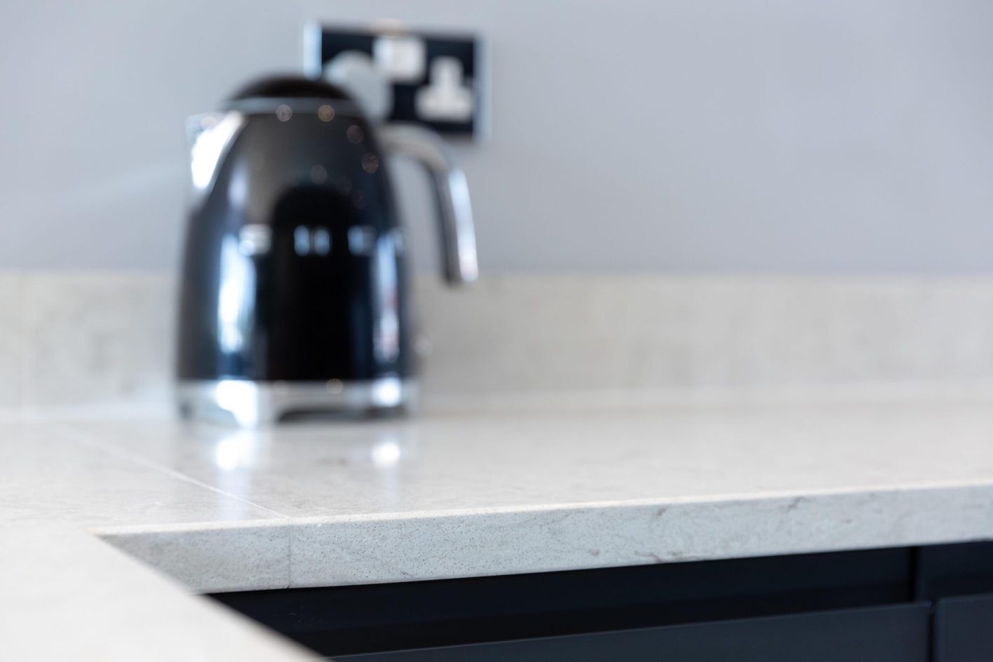 Grey Drift Quartz worktop close-up with kettle in the background showing a light grey stone-effect finish
