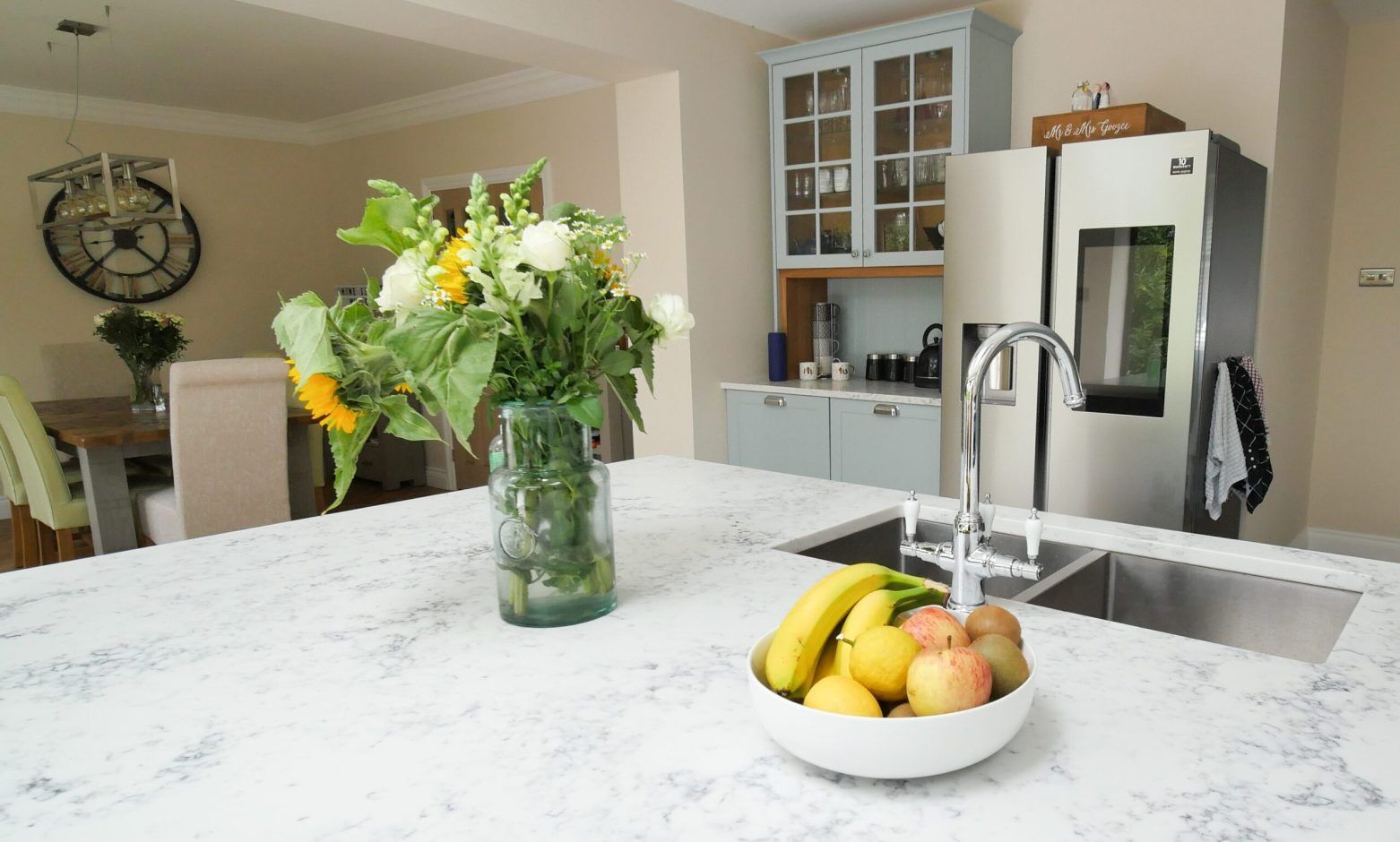 Arabescato Quartz island worktop with flowers and fruit bowl beside a sink, showing grey veining