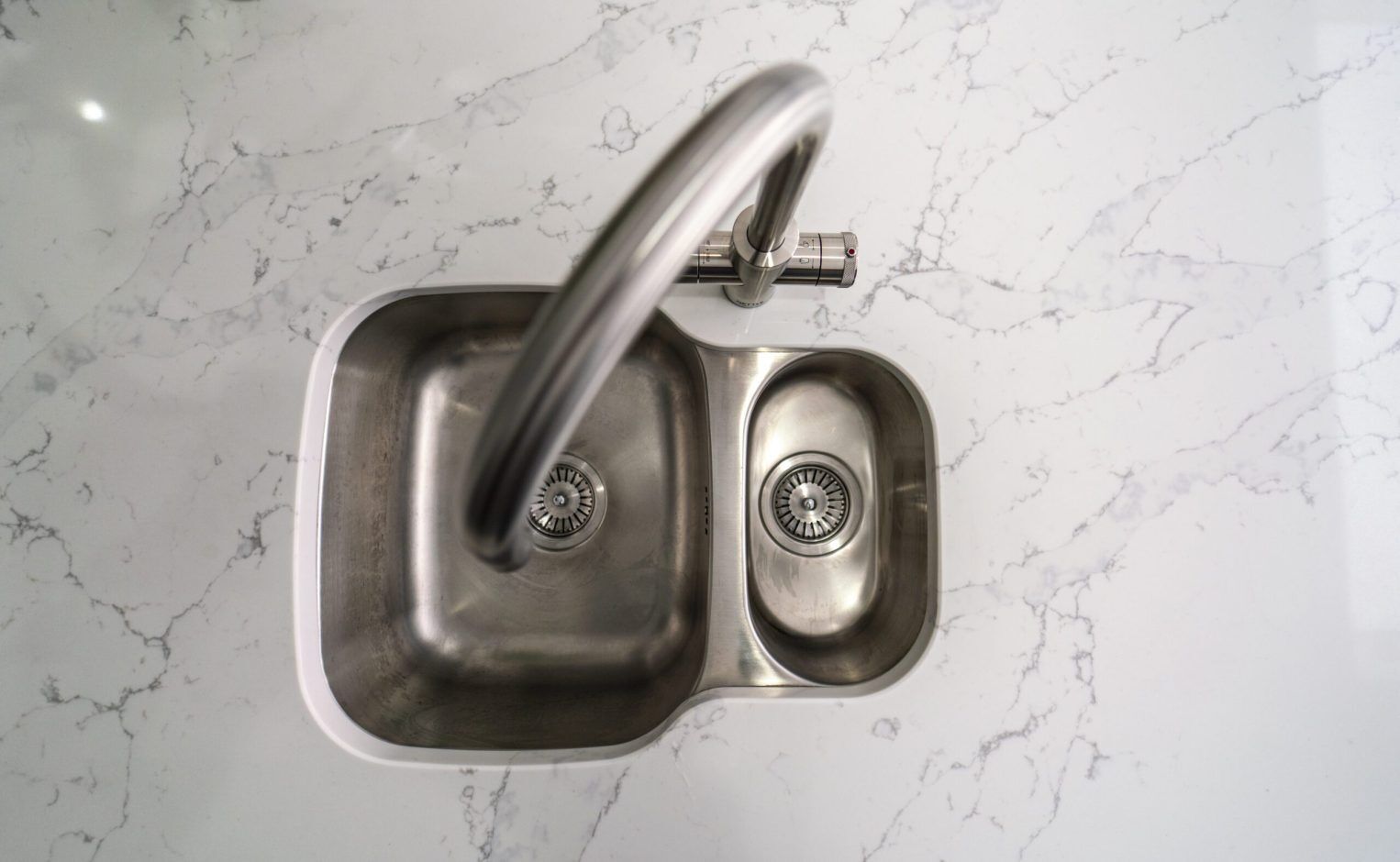 Close up of chrome tap fitted into White Calacatta Quartz worktop with grey veining