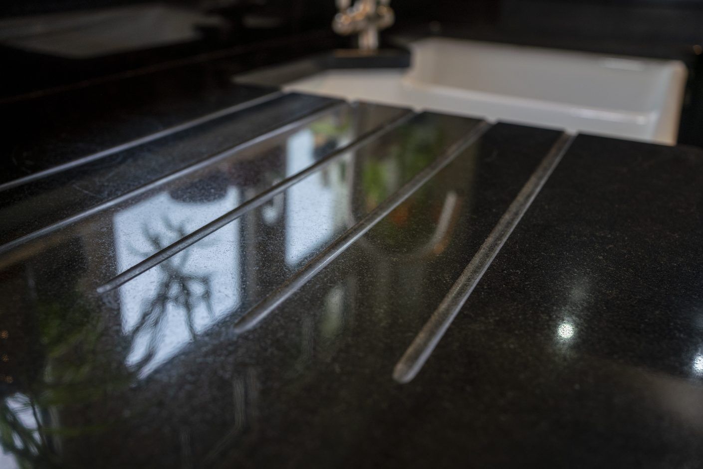 Close up of Absolute Black Granite worktop showing precision cut drainer grooves with reflections on the polished surface near the sink.