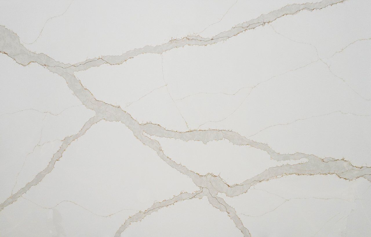 Britannicca Calacatta Quartz slab close-up showing warm grey veining with soft branching movement on a bright white base