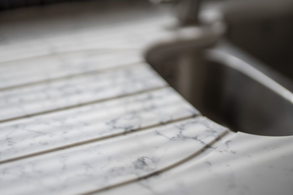 Close-up of Arabescato Quartz drainer grooves beside a sink showing grey veining across the surface