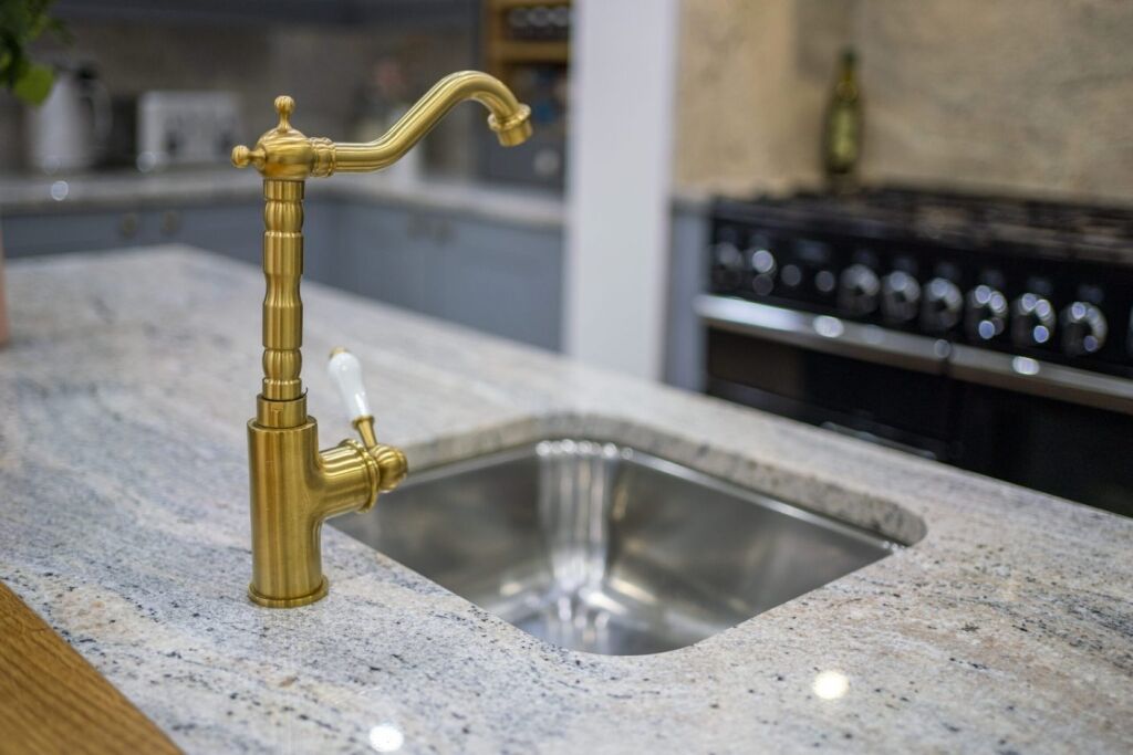 Kitchen sink detail with brass tap set into an Ivory Fantasy Granite worktop, highlighting the Granite pattern and smooth polished finish.