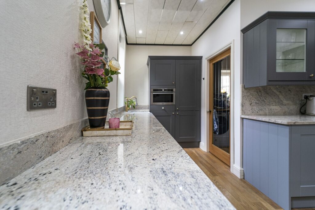 Perspective view along an Ivory Fantasy Granite worktop run showing the Granite pattern and polished edge, with flowers and a plant at the far end.